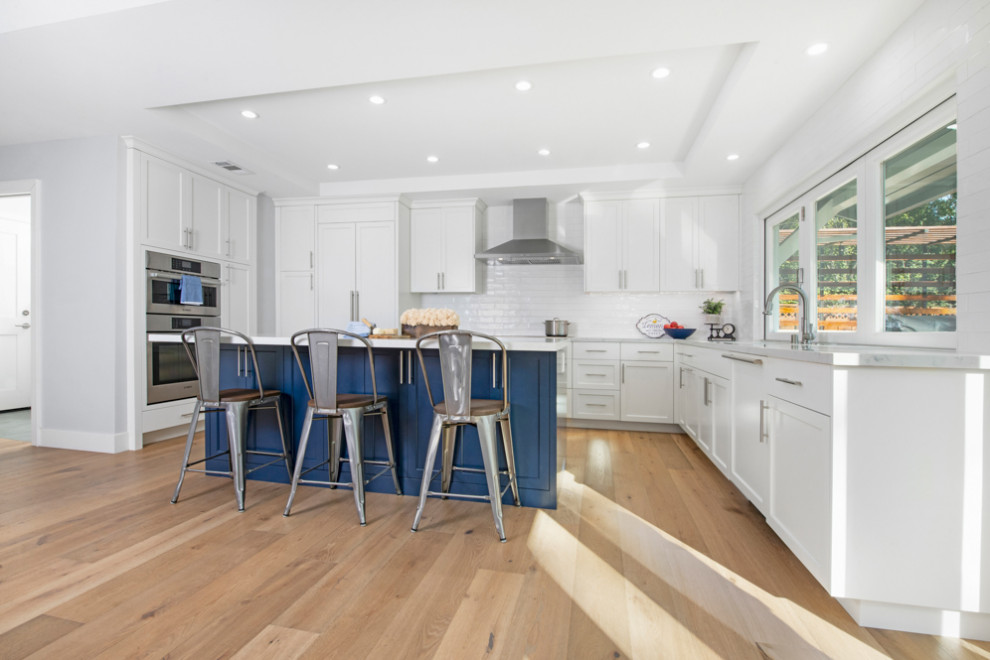 Photo of a mid-sized transitional u-shaped open plan kitchen in San Francisco with an undermount sink, shaker cabinets, white cabinets, quartz benchtops, white splashback, ceramic splashback, stainless steel appliances, light hardwood floors, with island, brown floor, white benchtop and coffered.