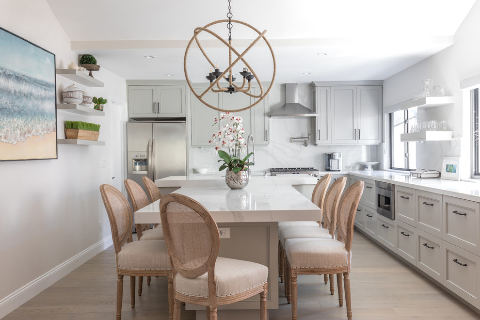 Mid-sized transitional l-shaped kitchen in Orange County with grey cabinets, quartz benchtops, white splashback, marble splashback, stainless steel appliances, light hardwood floors, with island, white benchtop, a farmhouse sink, recessed-panel cabinets and beige floor.