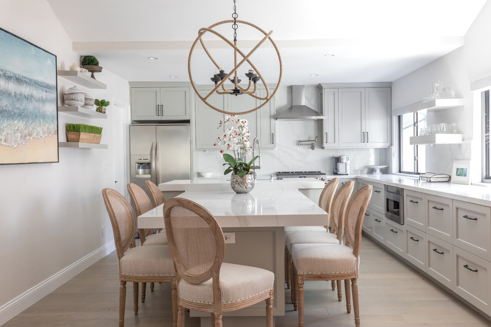 Example of a mid-sized transitional l-shaped light wood floor and beige floor kitchen design in Orange County with gray cabinets, quartz countertops, white backsplash, marble backsplash, stainless steel appliances, an island, white countertops, a farmhouse sink and recessed-panel cabinets