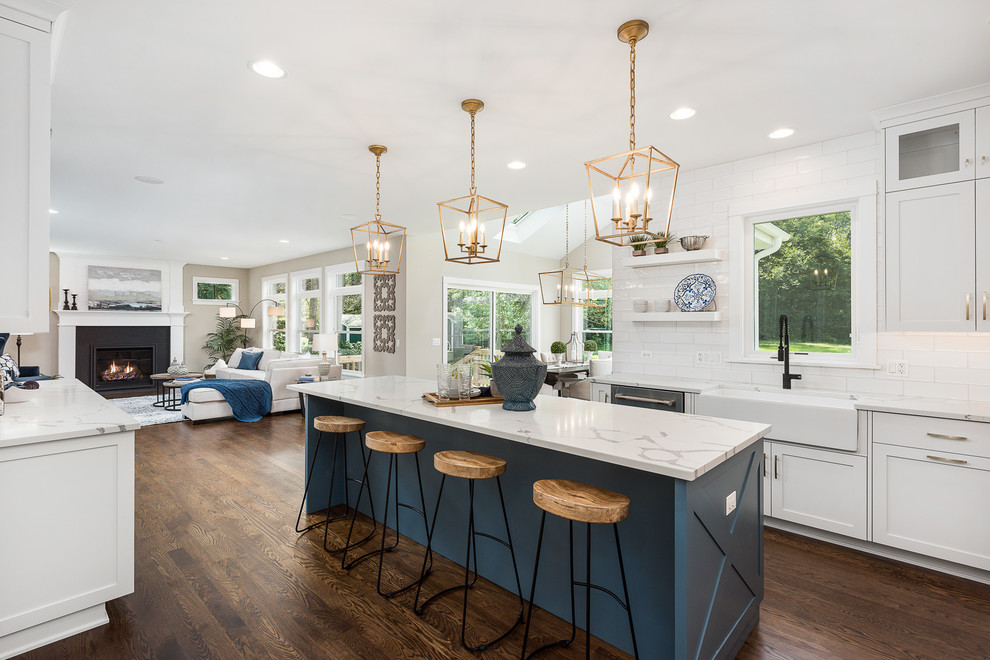 Example of a large transitional l-shaped dark wood floor and brown floor open concept kitchen design in Chicago with a farmhouse sink, shaker cabinets, white cabinets, quartzite countertops, white backsplash, subway tile backsplash, stainless steel appliances, an island and white countertops
