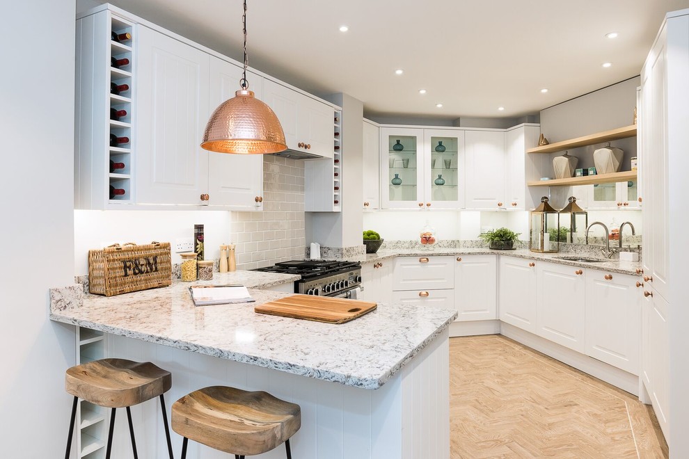 Design ideas for a transitional kitchen in London with white cabinets, grey splashback, stainless steel appliances, light hardwood floors, a peninsula, an undermount sink, raised-panel cabinets, subway tile splashback, beige floor and multi-coloured benchtop.