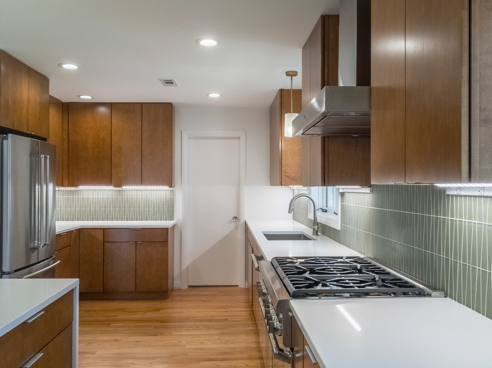 Inspiration for a large midcentury l-shaped open plan kitchen in Raleigh with an undermount sink, flat-panel cabinets, medium wood cabinets, quartz benchtops, green splashback, glass tile splashback, stainless steel appliances, medium hardwood floors and with island.
