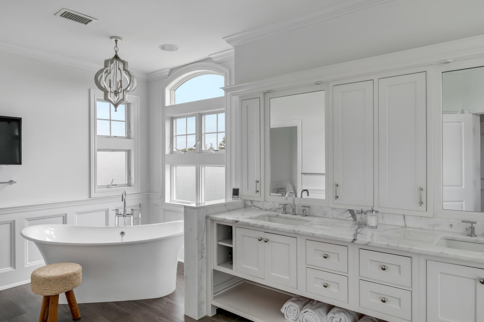 Traditional master bathroom in New York with beaded inset cabinets, white cabinets, a freestanding tub, white walls, dark hardwood floors, an undermount sink, marble benchtops, brown floor and white benchtops.