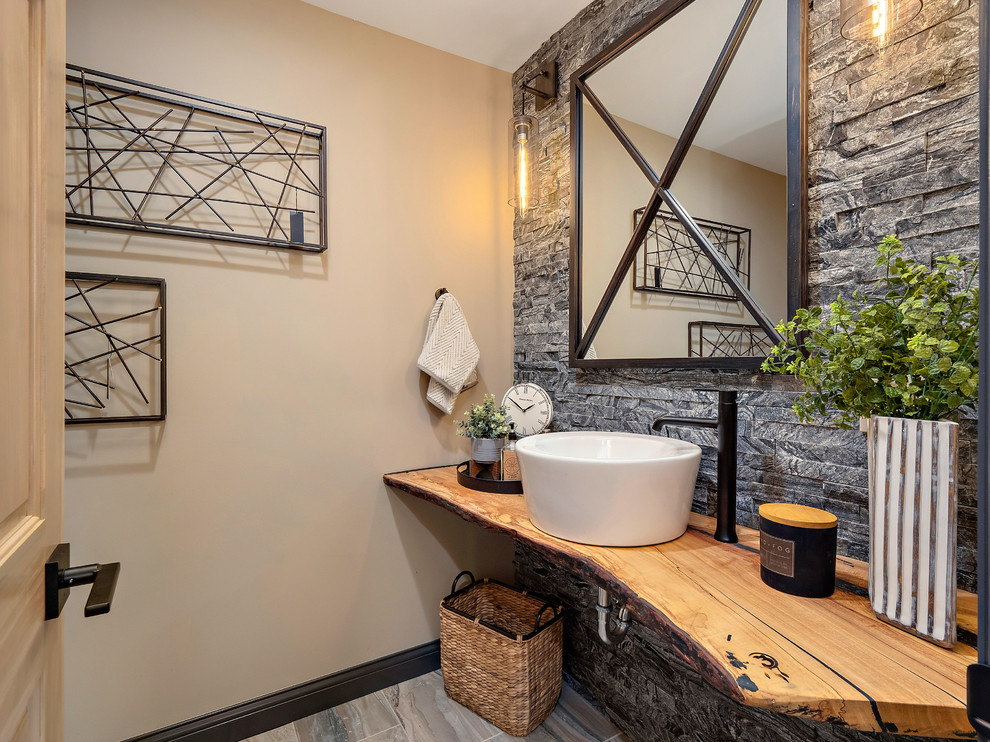 Inspiration for a country powder room in Other with open cabinets, medium wood cabinets, gray tile, stone tile, beige walls, a vessel sink, wood benchtops, grey floor and brown benchtops.