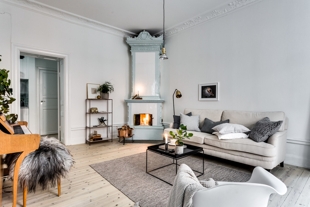 Design ideas for a large scandinavian enclosed living room in Stockholm with a music area, white walls, light hardwood floors, a corner fireplace and no tv.