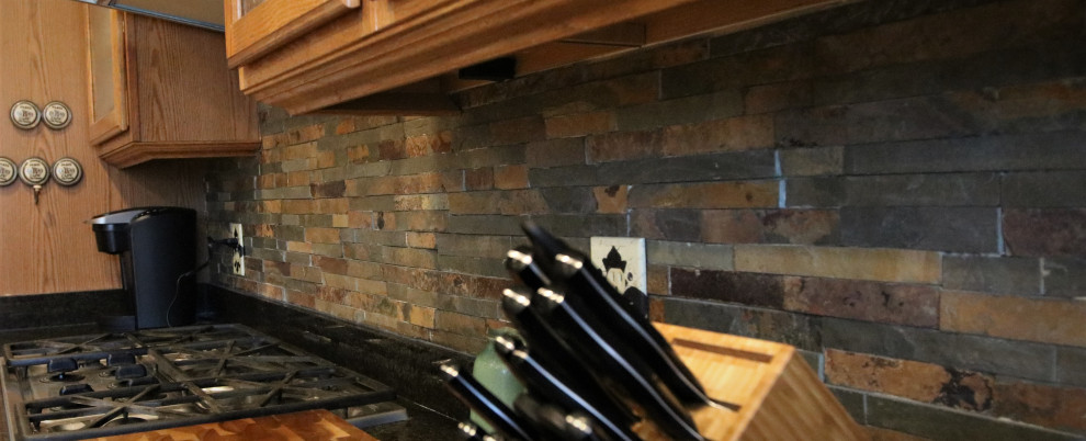 Inspiration for a mid-sized rustic l-shaped eat-in kitchen remodel with glass-front cabinets, light wood cabinets, granite countertops, multicolored backsplash, stone tile backsplash, stainless steel appliances, an island and black countertops