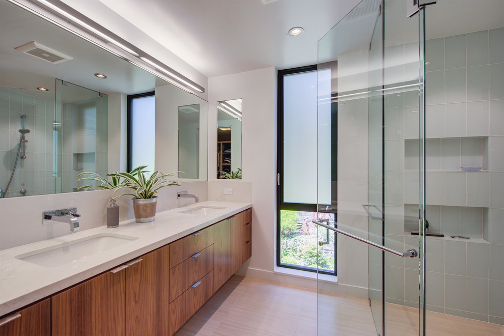 Photo of a small contemporary master bathroom with flat-panel cabinets, medium wood cabinets, a corner shower, a wall-mount toilet, blue tile, glass tile, white walls, porcelain floors, an undermount sink, engineered quartz benchtops, grey floor, a hinged shower door and white benchtops.