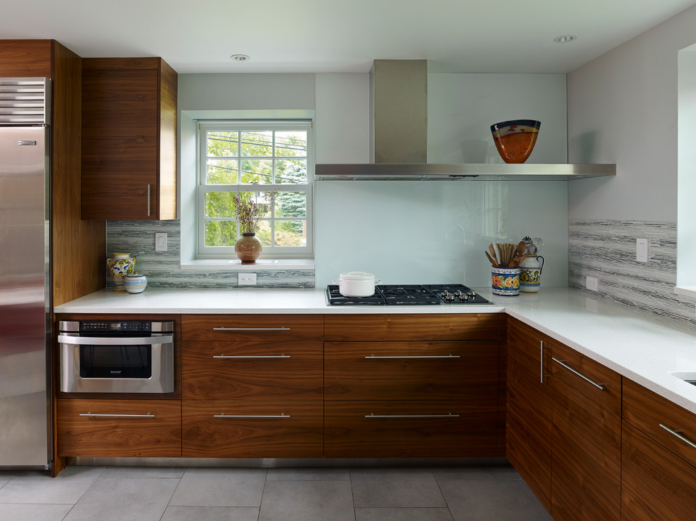 This is an example of a contemporary u-shaped eat-in kitchen in Philadelphia with an undermount sink, flat-panel cabinets, medium wood cabinets, quartz benchtops, white splashback, glass sheet splashback and stainless steel appliances.