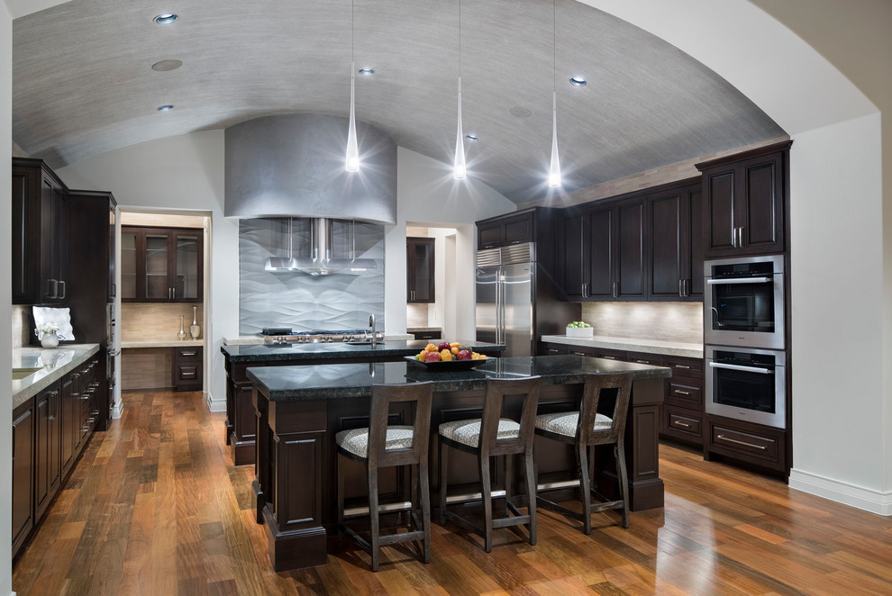 Inspiration for a transitional u-shaped kitchen in Austin with an undermount sink, raised-panel cabinets, dark wood cabinets, beige splashback, stainless steel appliances, dark hardwood floors, multiple islands, brown floor and black benchtop.