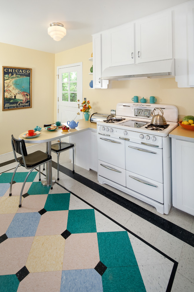 This is an example of a mid-sized midcentury u-shaped kitchen in Santa Barbara with a double-bowl sink, shaker cabinets, white cabinets, laminate benchtops, white appliances, linoleum floors, with island, multi-coloured floor and white benchtop.