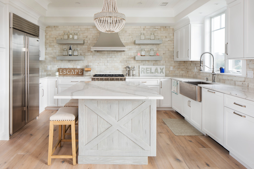 Photo of a mid-sized beach style l-shaped eat-in kitchen in New York with a farmhouse sink, white cabinets, quartz benchtops, beige splashback, ceramic splashback, stainless steel appliances, light hardwood floors, with island and brown floor.