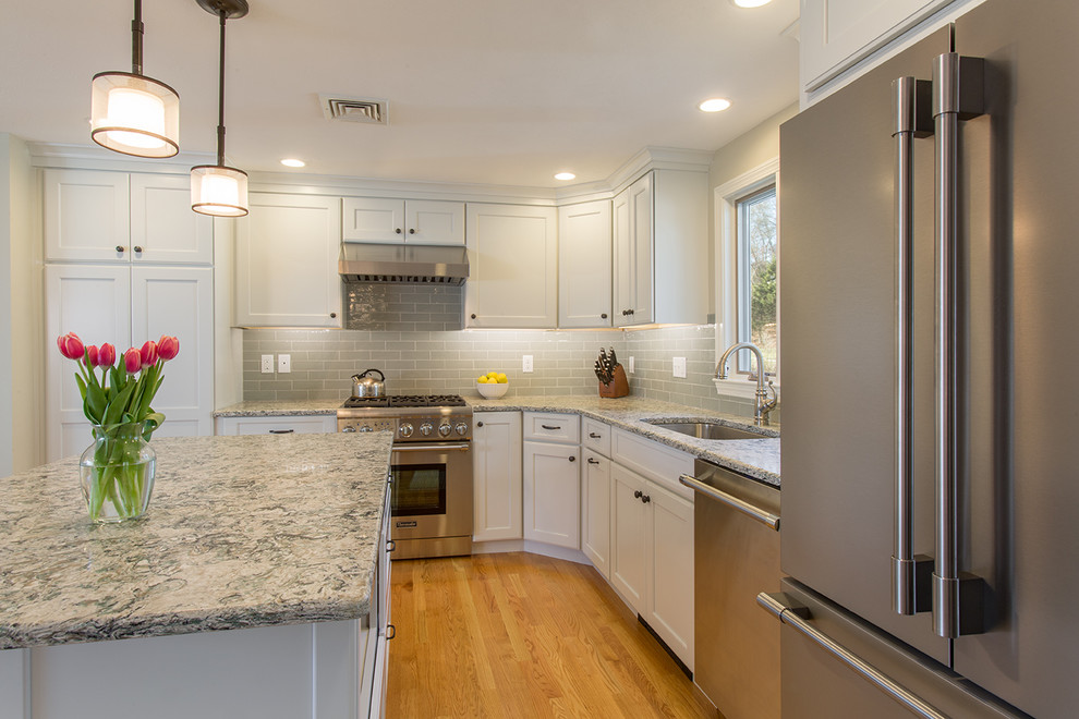 Example of a mid-sized transitional l-shaped medium tone wood floor eat-in kitchen design in Boston with an undermount sink, recessed-panel cabinets, white cabinets, quartz countertops, green backsplash, ceramic backsplash, stainless steel appliances and an island