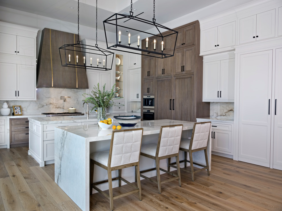 Example of a huge transitional l-shaped light wood floor, brown floor and tray ceiling kitchen pantry design in Miami with a farmhouse sink, shaker cabinets, white cabinets, solid surface countertops, white backsplash, porcelain backsplash, stainless steel appliances, two islands and white countertops