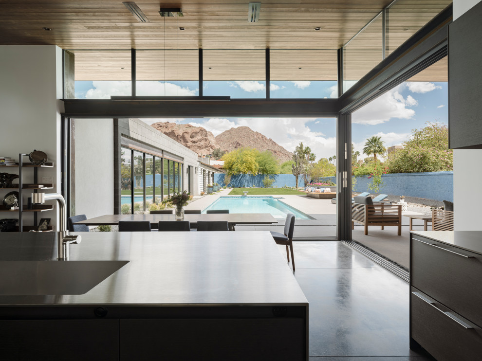 Minimalist l-shaped concrete floor and wood ceiling open concept kitchen photo in Phoenix with an integrated sink, flat-panel cabinets, black cabinets, stainless steel countertops, stainless steel appliances and an island
