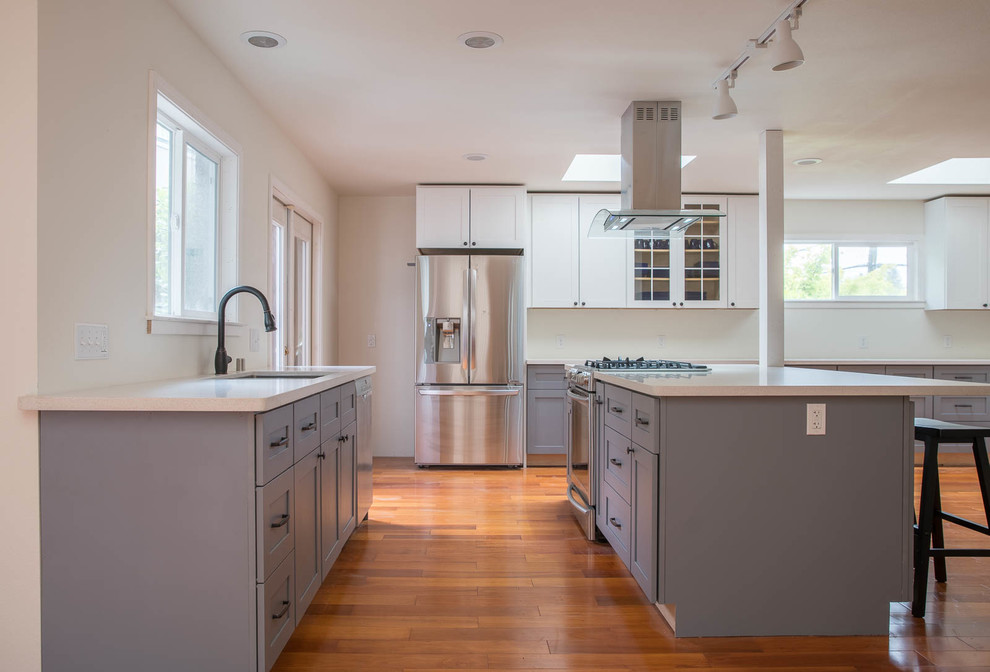 Large midcentury l-shaped eat-in kitchen in San Francisco with quartz benchtops, white splashback, with island, an undermount sink, shaker cabinets, grey cabinets, stainless steel appliances, medium hardwood floors, brown floor and white benchtop.