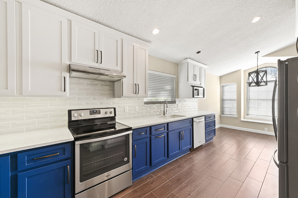 Open concept kitchen - large transitional l-shaped vinyl floor and brown floor open concept kitchen idea in Jacksonville with an undermount sink, shaker cabinets, blue cabinets, quartzite countertops, white backsplash, ceramic backsplash, stainless steel appliances and a peninsula