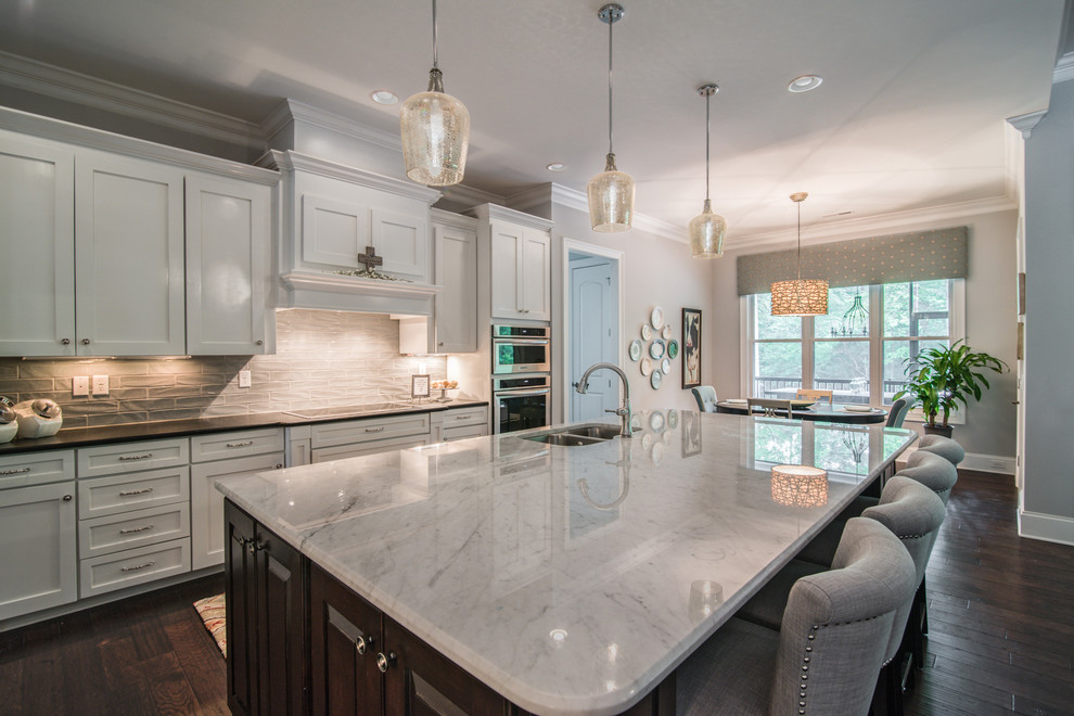 Photo of an expansive transitional l-shaped eat-in kitchen in Charlotte with a double-bowl sink, shaker cabinets, white cabinets, marble benchtops, grey splashback, subway tile splashback, stainless steel appliances, dark hardwood floors, with island and brown floor.