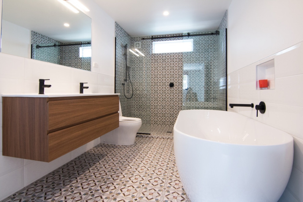 Пример оригинального дизайна: большая главная, серо-белая ванная комната в стиле ретро с фасадами цвета дерева среднего тона, отдельно стоящей ванной, душевой комнатой, унитазом-моноблоком, разноцветной плиткой, керамической плиткой, разноцветными стенами, полом из керамической плитки, накладной раковиной, столешницей из ламината, разноцветным полом, открытым душем, белой столешницей, акцентной стеной, тумбой под две раковины и подвесной тумбой