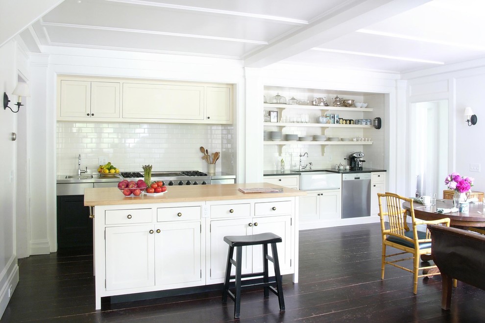 Photo of a mid-sized country single-wall eat-in kitchen in New York with white cabinets, with island, a farmhouse sink, stainless steel benchtops, white splashback, subway tile splashback, stainless steel appliances, dark hardwood floors, beaded inset cabinets and brown floor.