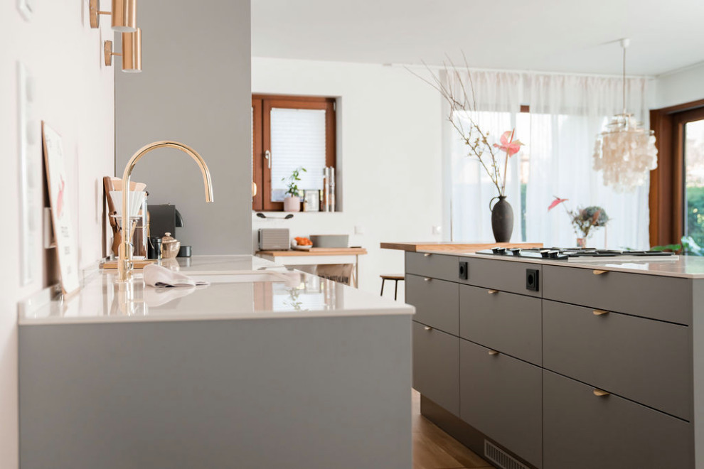 This is an example of a mid-sized scandinavian galley eat-in kitchen in Other with an undermount sink, flat-panel cabinets, grey cabinets, pink splashback, black appliances, light hardwood floors, with island and white benchtop.
