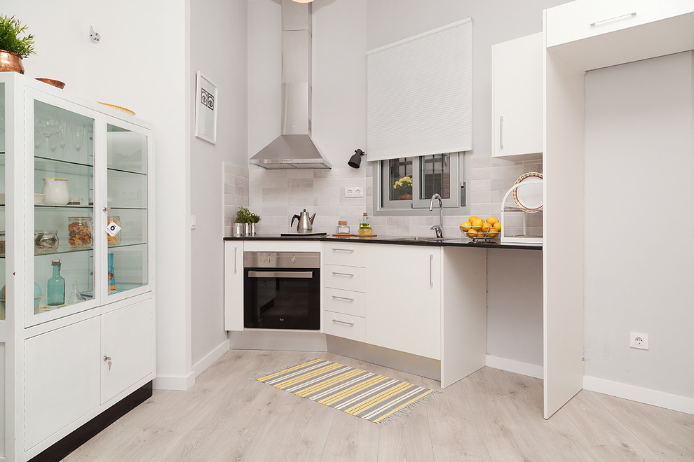 This is an example of a mid-sized contemporary single-wall open plan kitchen in Barcelona with flat-panel cabinets, light hardwood floors, no island, white cabinets, grey splashback, ceramic splashback and stainless steel appliances.