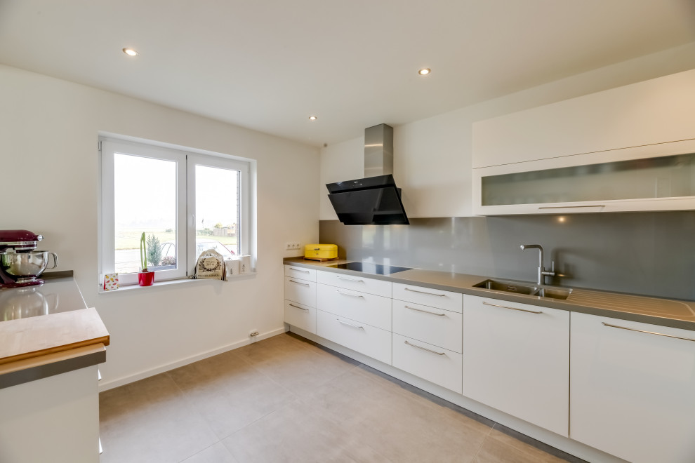 Moderne Küche in L-Form mit flächenbündigen Schrankfronten, weißen Schränken, Küchenrückwand in Grau, Keramikboden, Kücheninsel, grauem Boden und grauer Arbeitsplatte in Düsseldorf