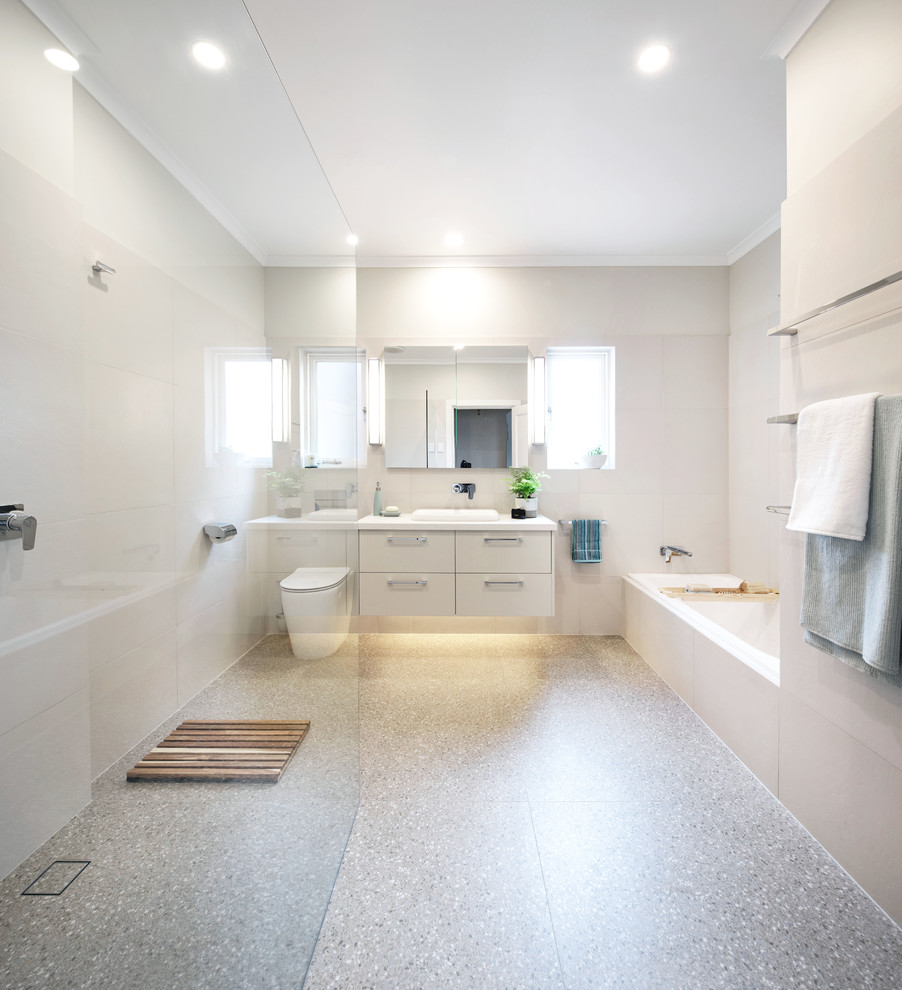This is an example of a mid-sized modern 3/4 bathroom in Melbourne with flat-panel cabinets, beige cabinets, a drop-in tub, a curbless shower, a one-piece toilet, beige tile, porcelain tile, beige walls, terrazzo floors, a drop-in sink, quartzite benchtops, multi-coloured floor, an open shower and white benchtops.