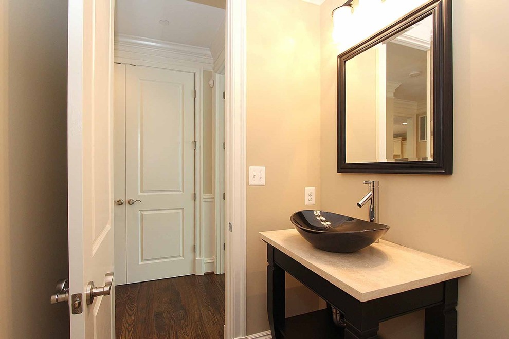 This is an example of a mid-sized traditional powder room in DC Metro with open cabinets, dark wood cabinets, a one-piece toilet, beige walls, medium hardwood floors, a vessel sink and travertine benchtops.