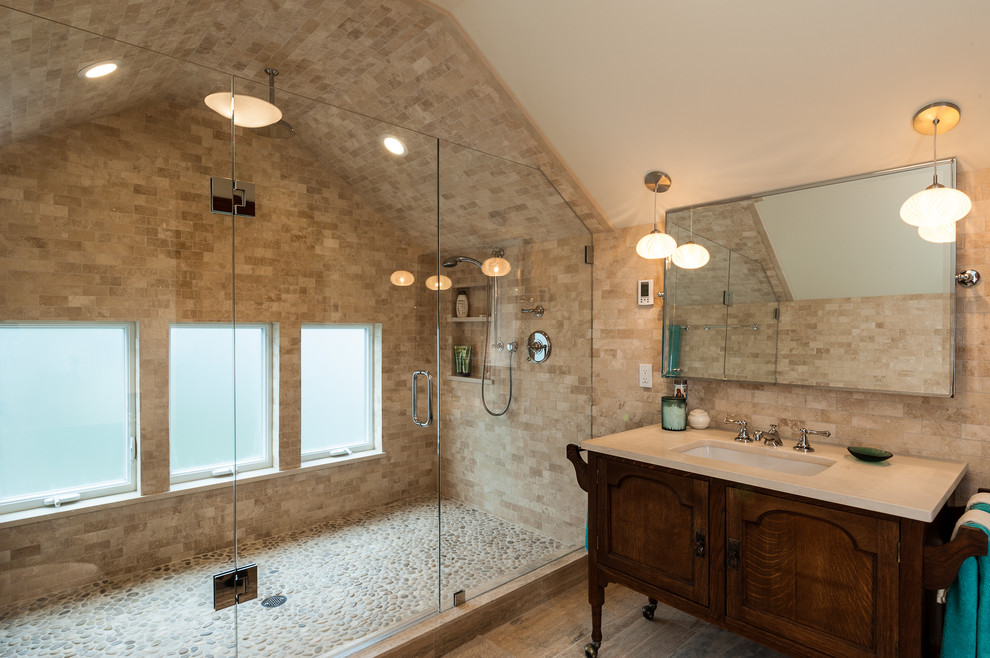 This is an example of a traditional bathroom in Seattle with an undermount sink, dark wood cabinets, an alcove shower, beige tile, pebble tile floors, travertine and recessed-panel cabinets.