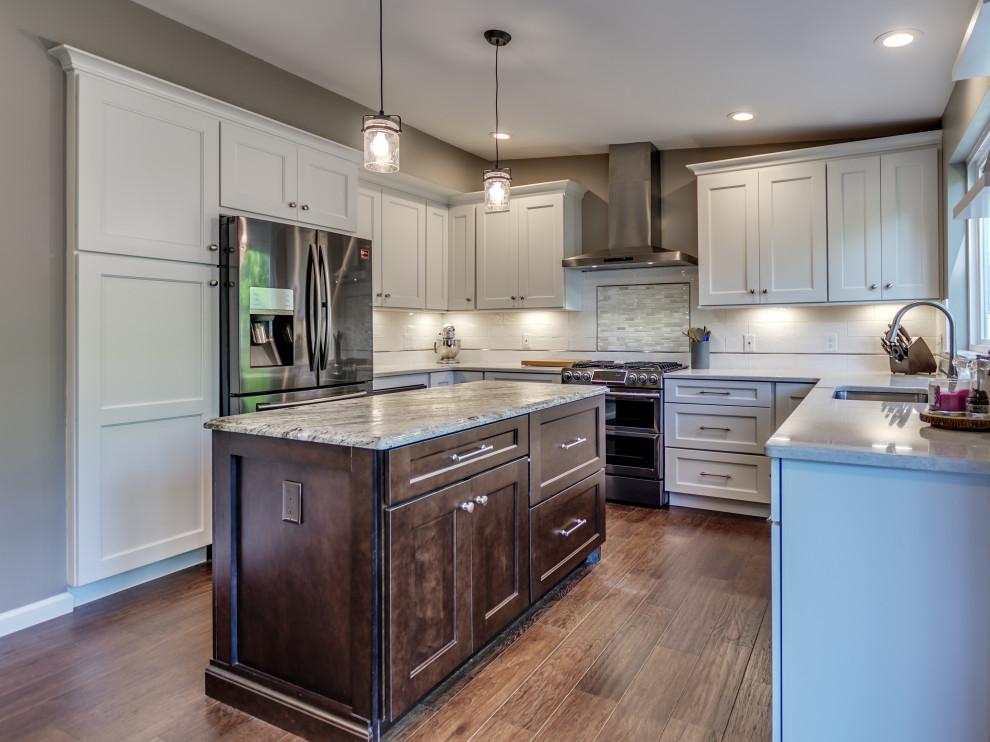 Example of a mid-sized transitional u-shaped brown floor eat-in kitchen design in St Louis with white cabinets, white backsplash, subway tile backsplash, stainless steel appliances, an island, granite countertops and multicolored countertops