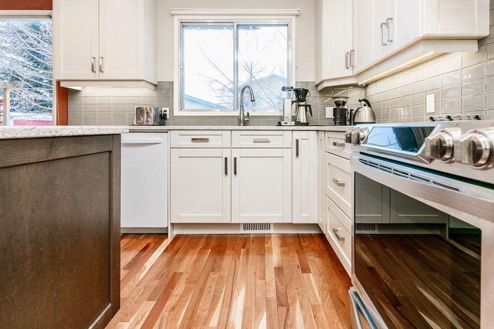 Inspiration for a large transitional u-shaped medium tone wood floor eat-in kitchen remodel in Calgary with an undermount sink, shaker cabinets, white cabinets, gray backsplash, glass tile backsplash, stainless steel appliances, an island and marble countertops