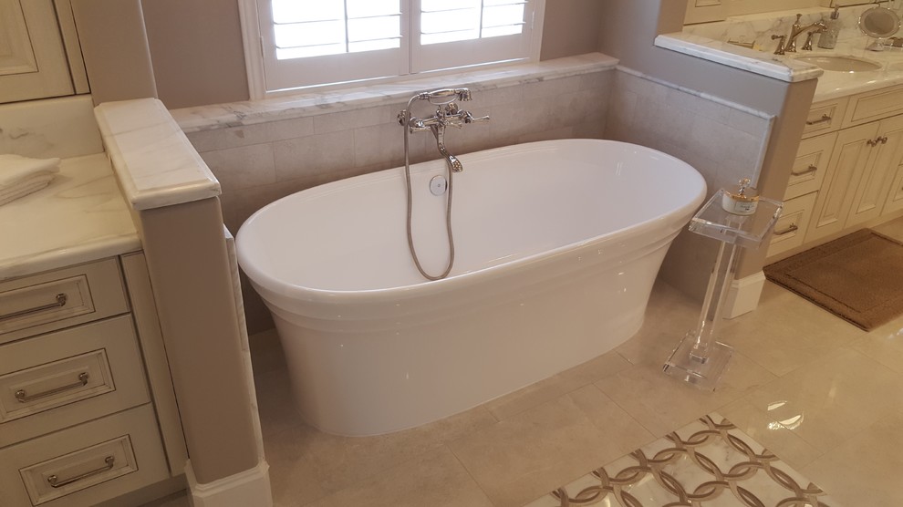 This is an example of a mid-sized traditional master bathroom in Houston with raised-panel cabinets, beige cabinets, a freestanding tub, an alcove shower, a one-piece toilet, beige tile, marble, beige walls, marble floors, a drop-in sink, marble benchtops, beige floor and a hinged shower door.