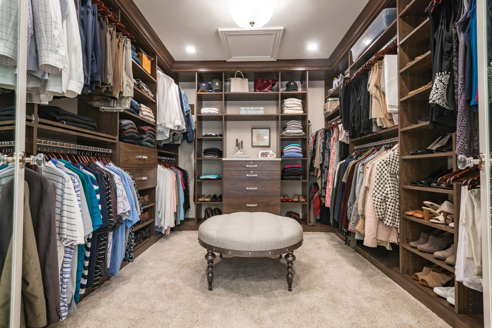 Large traditional gender-neutral walk-in wardrobe in Chicago with open cabinets, dark wood cabinets, carpet and beige floor.