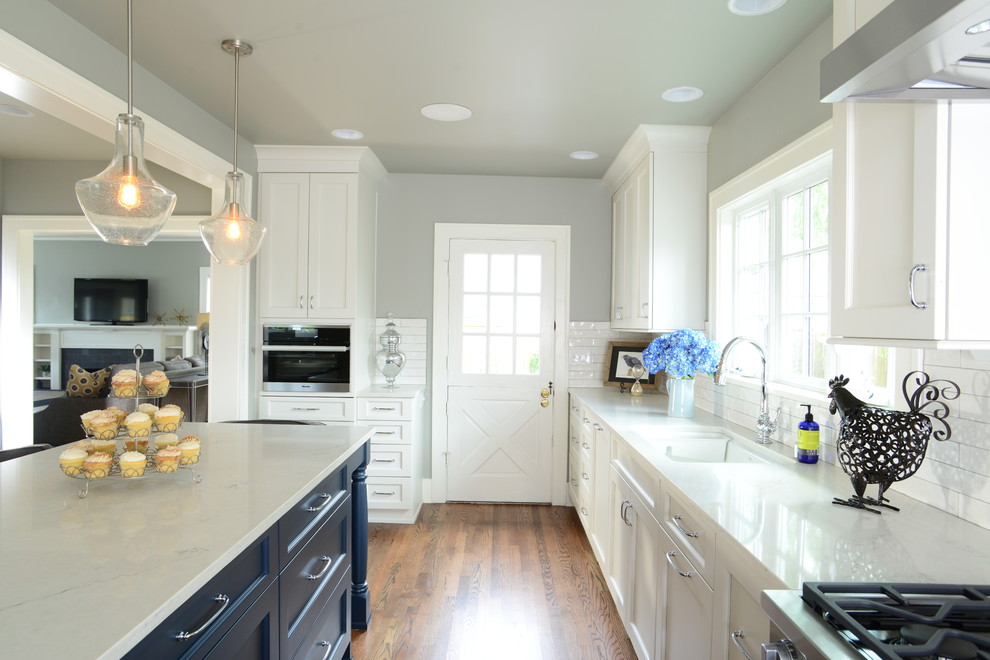 Inspiration for a large transitional single-wall medium tone wood floor eat-in kitchen remodel in Seattle with an undermount sink, shaker cabinets, white cabinets, quartz countertops, white backsplash, subway tile backsplash, paneled appliances and an island