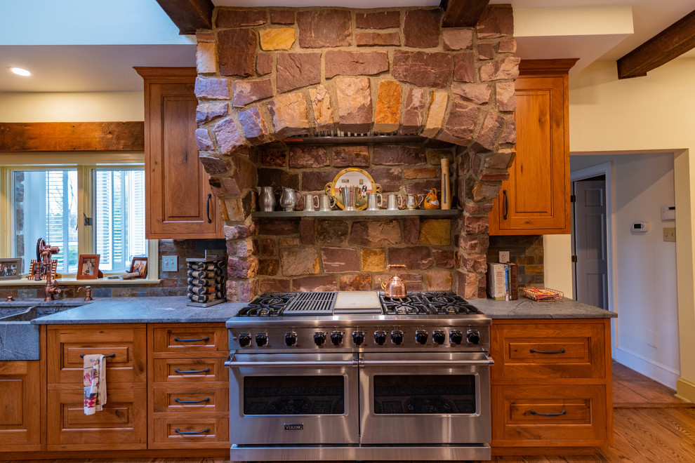 Example of a large mountain style l-shaped medium tone wood floor and brown floor eat-in kitchen design in Philadelphia with a farmhouse sink, raised-panel cabinets, distressed cabinets, soapstone countertops, multicolored backsplash, stone tile backsplash, stainless steel appliances, an island and blue countertops