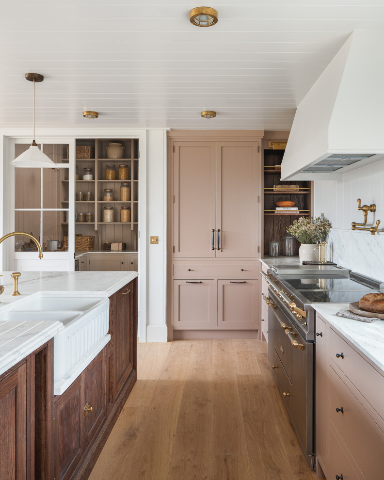 Photo of a mid-sized country kitchen in Other with a farmhouse sink, recessed-panel cabinets, pink cabinets, granite benchtops, white splashback, granite splashback, stainless steel appliances, light hardwood floors, with island and white benchtop.