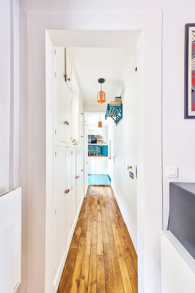 Photo of a mid-sized midcentury hallway in Paris with white walls, medium hardwood floors and brown floor.