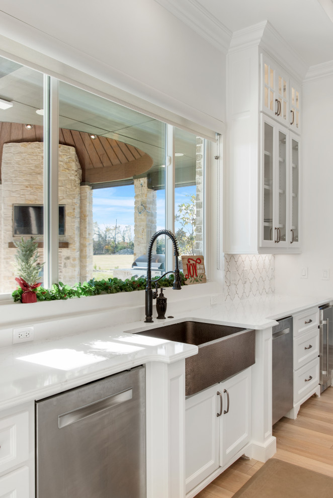 Foto på ett stort vit kök, med en rustik diskho, luckor med infälld panel, vita skåp, bänkskiva i kvartsit, vitt stänkskydd, stänkskydd i stenkakel, integrerade vitvaror, ljust trägolv och en köksö