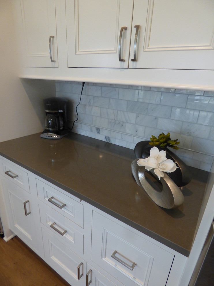 Inspiration for a large transitional l-shaped light wood floor eat-in kitchen remodel with an undermount sink, recessed-panel cabinets, white cabinets, quartz countertops, white backsplash, subway tile backsplash, stainless steel appliances and an island