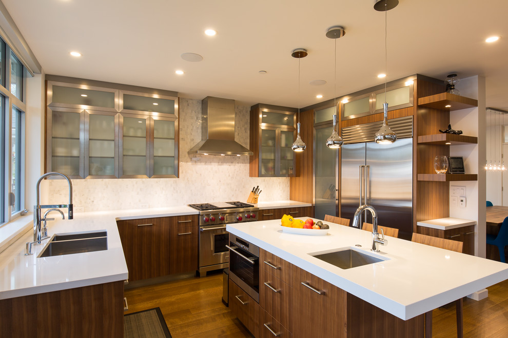 This is an example of a large contemporary u-shaped open plan kitchen in Vancouver with an undermount sink, flat-panel cabinets, medium wood cabinets, quartz benchtops, white splashback, porcelain splashback, stainless steel appliances, light hardwood floors and with island.