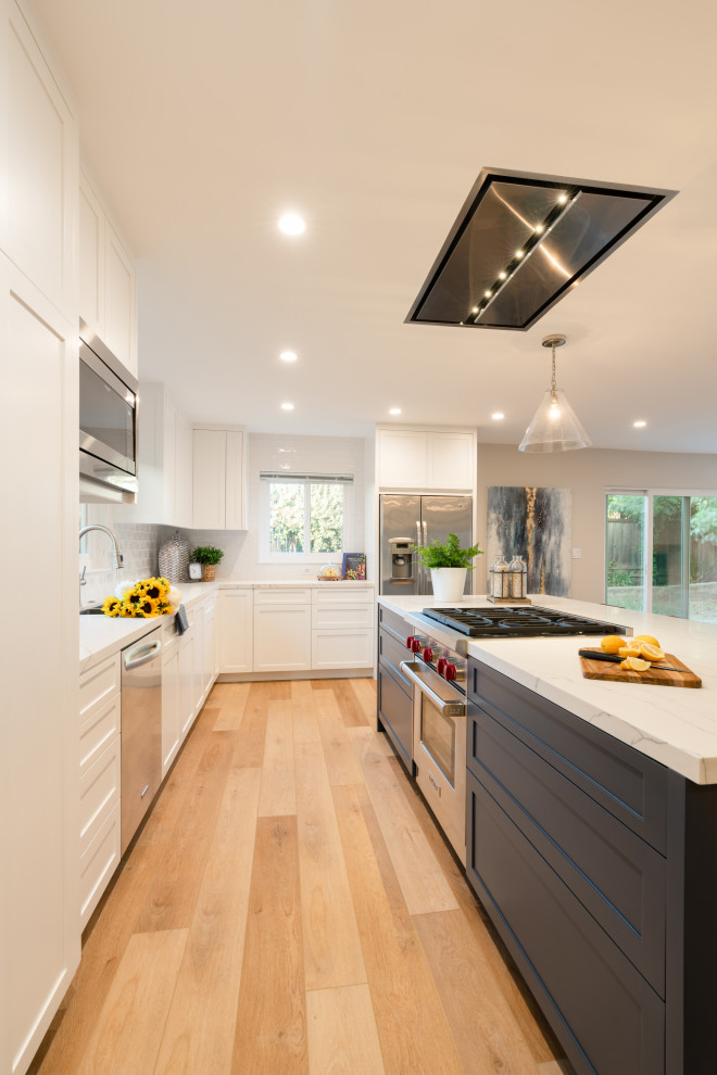 Inspiration for a mid-sized midcentury l-shaped eat-in kitchen in Santa Barbara with an undermount sink, shaker cabinets, white cabinets, quartz benchtops, white splashback, subway tile splashback, stainless steel appliances, vinyl floors, with island, brown floor and white benchtop.