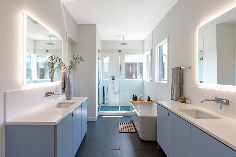 Photo of a contemporary bathroom in Austin with flat-panel cabinets, blue cabinets, a freestanding tub, an alcove shower, white tile, white walls, an undermount sink, black floor, a hinged shower door, white benchtops, a double vanity and a freestanding vanity.