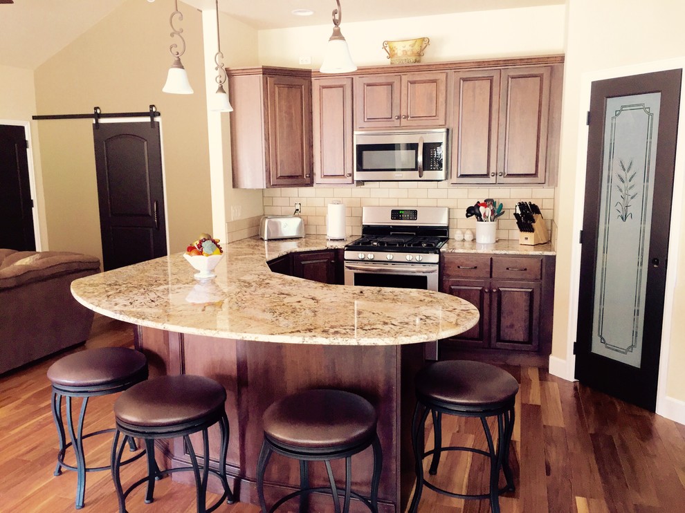 Example of a mid-sized l-shaped medium tone wood floor open concept kitchen design in Denver with an undermount sink, raised-panel cabinets, medium tone wood cabinets, granite countertops, beige backsplash, subway tile backsplash, stainless steel appliances and an island