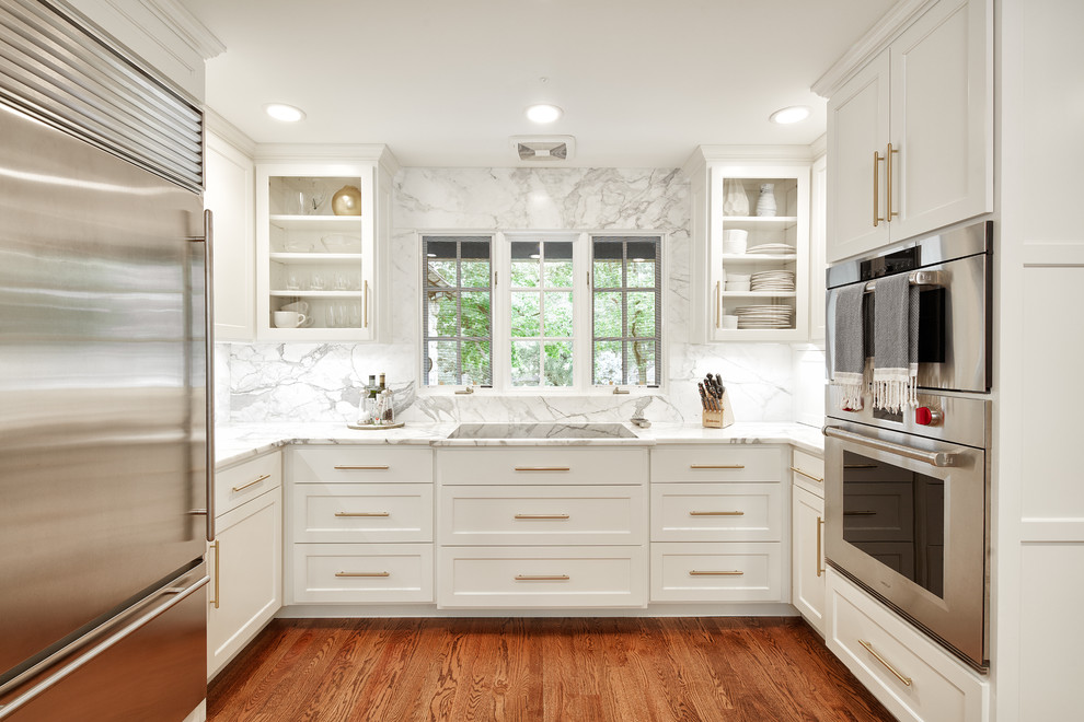 Large transitional u-shaped medium tone wood floor and brown floor eat-in kitchen photo with a farmhouse sink, shaker cabinets, white cabinets, marble countertops, white backsplash, marble backsplash, stainless steel appliances and an island