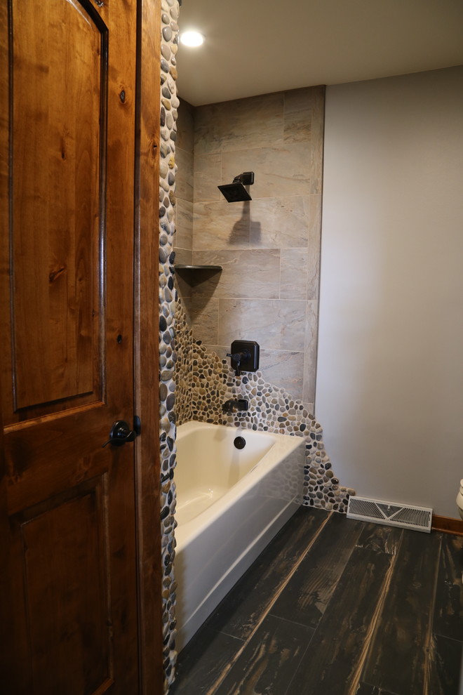 Photo of a mid-sized traditional master bathroom in Chicago with medium wood cabinets, a shower/bathtub combo, brown tile, pebble tile, grey walls, porcelain floors, granite benchtops and black floor.
