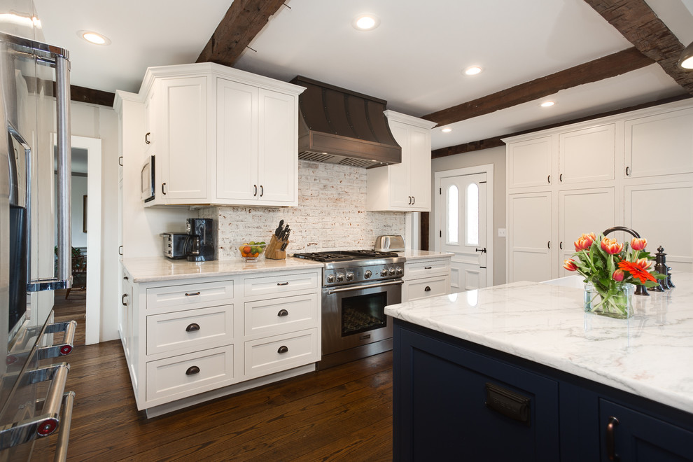 Photo of a mid-sized country l-shaped open plan kitchen in Providence with a farmhouse sink, beaded inset cabinets, white cabinets, quartzite benchtops, white splashback, brick splashback, stainless steel appliances, medium hardwood floors and with island.