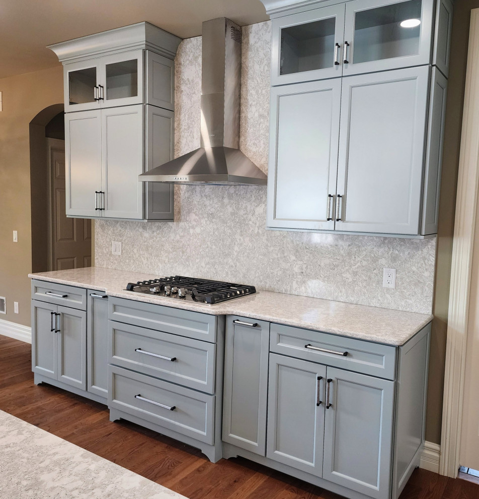 Mid-sized transitional medium tone wood floor and brown floor open concept kitchen photo with an undermount sink, shaker cabinets, quartz countertops, white backsplash, quartz backsplash, stainless steel appliances, an island and white countertops
