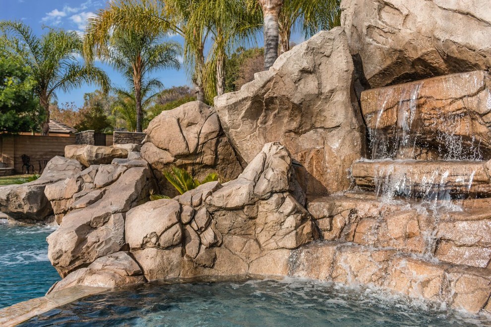 Photo of a large tropical backyard custom-shaped pool in Orange County with a water slide and concrete pavers.