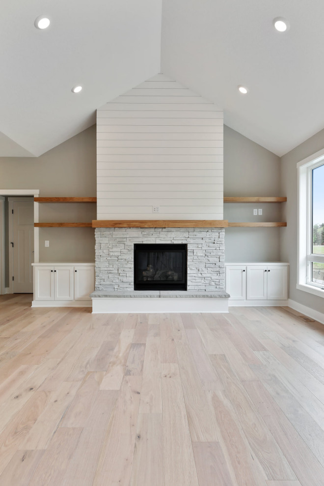 Large farmhouse open concept medium tone wood floor and vaulted ceiling living room photo in Minneapolis with gray walls, a standard fireplace, a stone fireplace and a wall-mounted tv