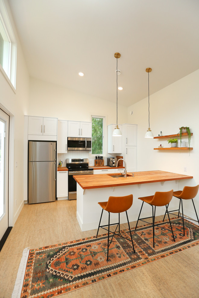 Inspiration for a small scandinavian galley kitchen in Seattle with an undermount sink, shaker cabinets, white cabinets, wood benchtops, white splashback, subway tile splashback, stainless steel appliances, cork floors and a peninsula.